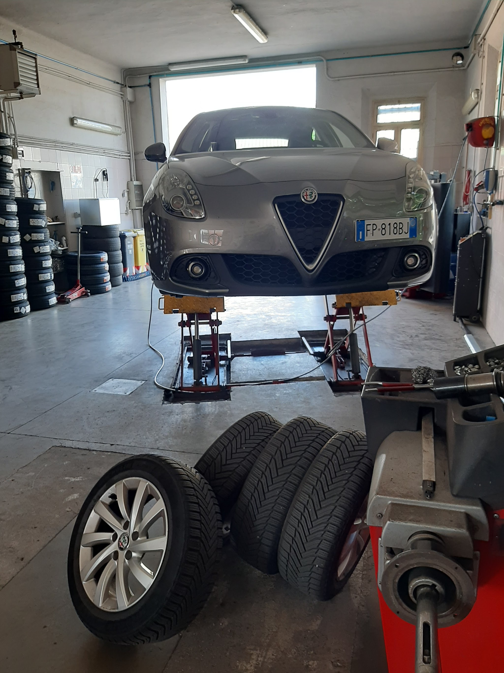 Auto in officina accanto a pile di pneumatici